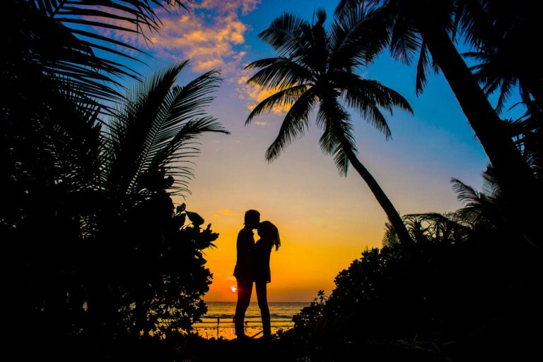 Best Wedding Venues in Port Douglas, Silhouette of a couple sharing a romantic moment on a tropical beach at sunset with palm trees.