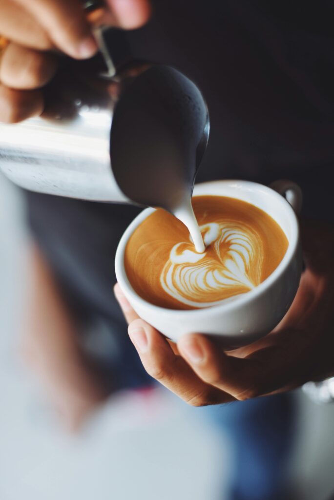 Best Cairns Cafes, Close-up of barista pouring milk to create stunning latte art in a coffee shop setting.