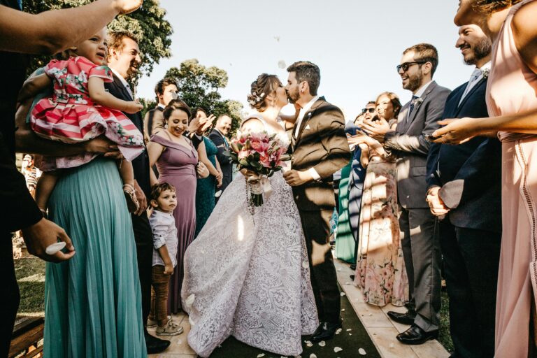 Port Douglas wedding venues, Outdoor wedding ceremony capturing a newlywed kiss as guests celebrate on a sunny day.