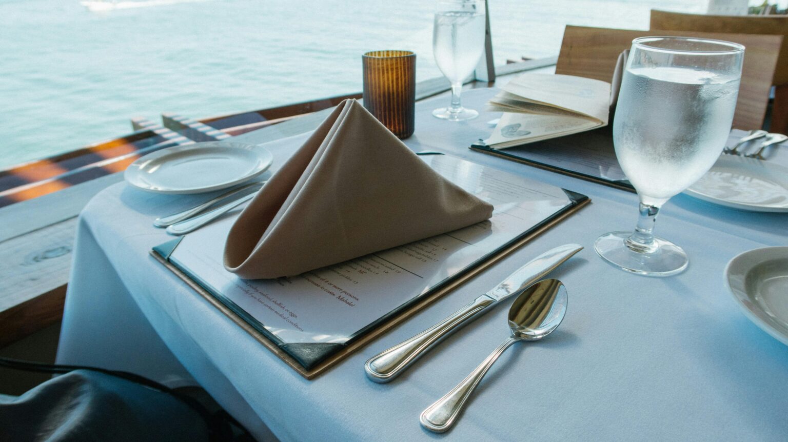 Best restaurants in Cairns, Luxurious dining table setup by the sea with elegant tableware and glassware.
