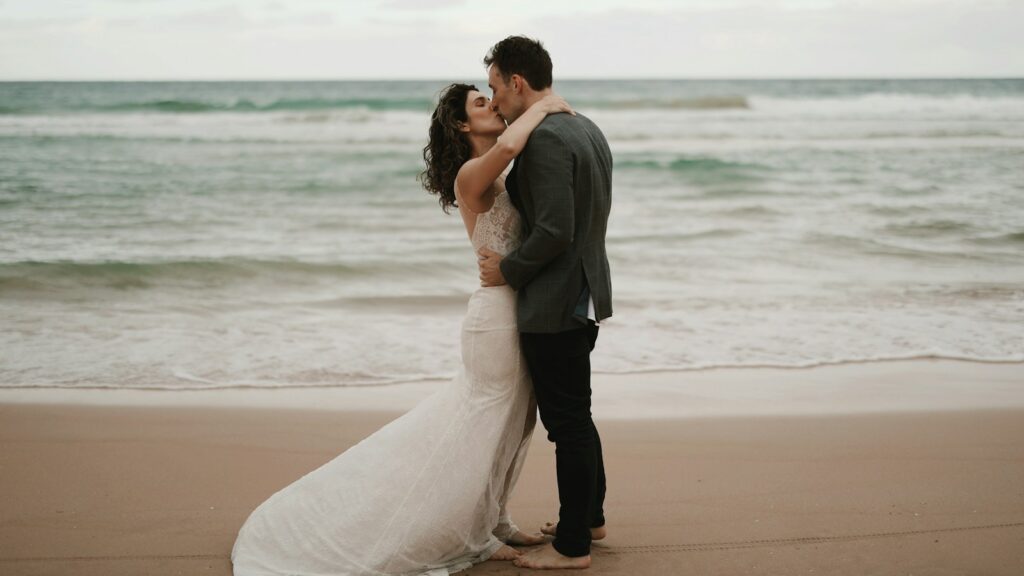a bride and groom kissing on the beach